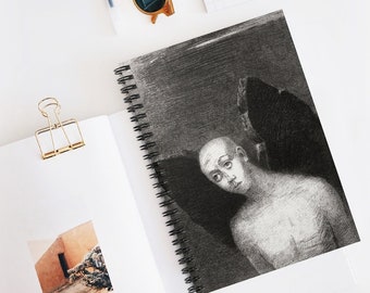 May include: A spiral-bound notebook featuring a grayscale illustration of a bald figure with a somber expression. The artwork is detailed with shading, creating depth. The notebook is open, revealing the drawing, and rests on a white surface.