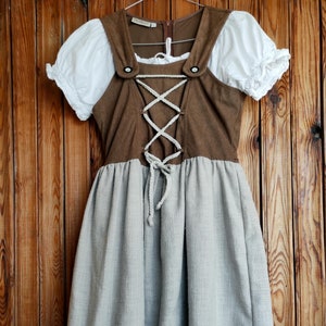 May include: A brown and white dirndl dress with a lace trim. The bodice is brown with a lace-up front and the skirt is white with a brown embroidered flower.