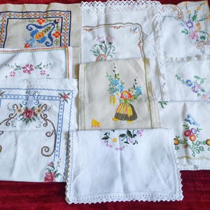 May include: A collection of eight vintage embroidered tablecloths in various floral patterns. The tablecloths are white with delicate lace edging and feature colourful floral embroidery.