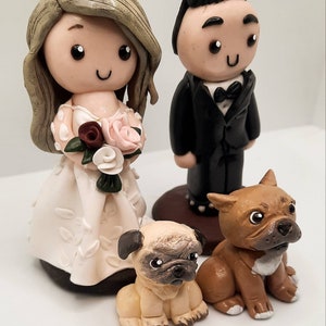May include: A wedding cake topper featuring a bride and groom with a white dress, black suit, and a brown and white dog and a brown dog.