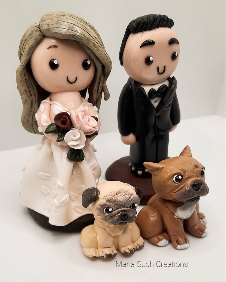 May include: A wedding cake topper featuring a bride and groom with a white dress, black suit, and a brown and white dog and a brown dog.