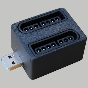 Könnte beinhalten: Ein schwarzer USB-Adapter mit zwei SNES-Controller-Ports. Der Adapter hat einen silbernen USB-Stecker.