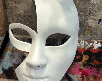 Può includere: Una maschera bianca da ballo in maschera, a mezza faccia, con una consistenza liscia. La maschera presenta ritagli per gli occhi, un naso e una bocca sorridente. Un nastro nero è attaccato per fissare la maschera. La maschera è progettata per costumi o scopi decorativi.