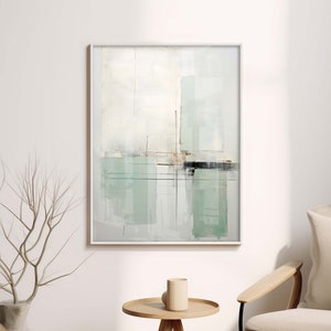 Puede incluir: Una pintura abstracta enmarcada con fondo blanco y pinceladas verdes y grises. La pintura está colgada en una pared blanca sobre una silla de madera y una pequeña mesa de madera.