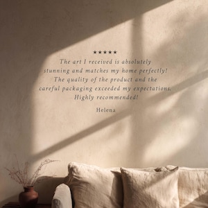 May include: A neutral-toned interior scene featuring a beige sofa with two pillows. The wall displays text: "The art I received is absolutely stunning and matches my home perfectly!" and "Highly recommended!" by Helena.
