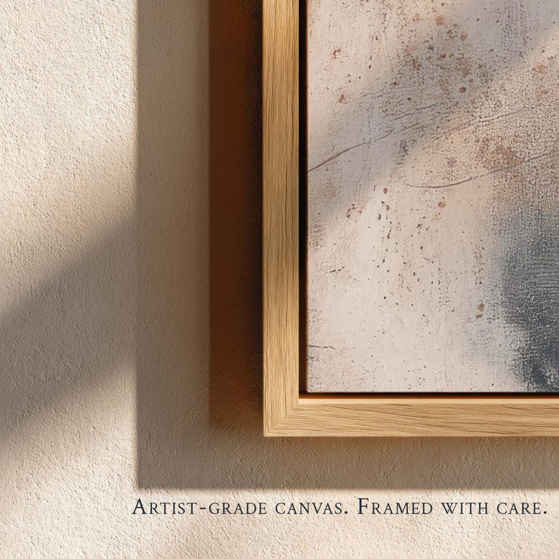 May include: A framed canvas with an abstract design in neutral tones of beige, gray, and white. The artwork is enclosed in a light-colored wooden frame. The text at the bottom reads: ARTIST-GRADE CANVAS. FRAMED WITH CARE.