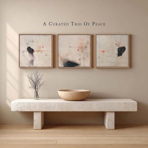May include: Three framed abstract paintings with neutral tones and black and red accents hang above a stone bench. A decorative bowl and a vase with branches sit on the bench. The text "A Curated Trio Of Peace" is above the paintings.