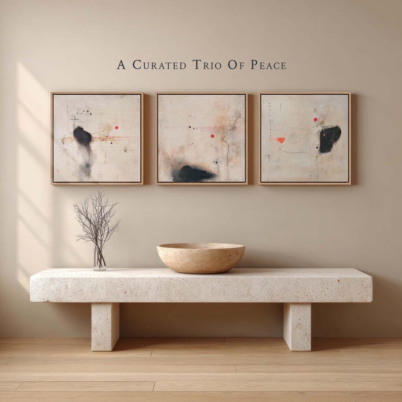 May include: Three framed abstract paintings with neutral tones and black and red accents hang above a stone bench. A decorative bowl and a vase with branches sit on the bench. The text "A Curated Trio Of Peace" is above the paintings.