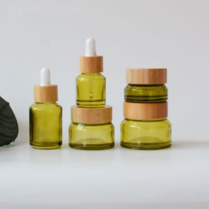 Könnte beinhalten: Eine Anordnung von kleinen, olivgrünen Glasflaschen mit Bambusdeckeln und weißen Pipetten. Die Flaschen sind in verschiedenen Größen und Formen angeordnet. Der Text "ONLY4CREATION" ist oben links sichtbar.