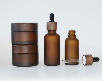 May include: Three brown glass bottles with wooden lids and a glass dropper. The bottles are on a white background.