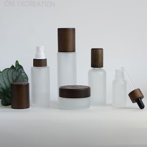 May include: A selection of frosted glass cosmetic containers with dark brown wooden lids. The set includes bottles, jars, and a dropper bottle. The text "ONLY4CREATION" is visible at the top of the image.