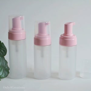 May include: Three frosted glass bottles with pink foam pump tops. The bottles are different sizes and are arranged from largest to smallest.
