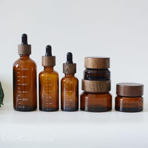 Op de afbeelding: Set van vijf amberkleurige glazen flessen met houten deksels. De flessen zijn gegradueerd in milliliter en variëren in grootte van 30 ml tot 100 ml.