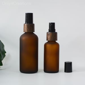 May include: Two amber glass bottles with frosted finish and black spray tops. The bottles have wooden caps. The smaller bottle is on the right and the larger bottle is on the left.