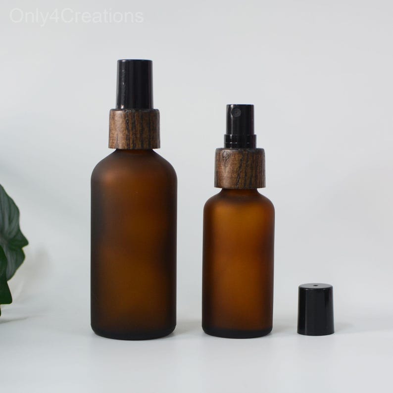 May include: Two amber glass bottles with frosted finish and black spray tops. The bottles have wooden caps. The smaller bottle is on the right and the larger bottle is on the left.