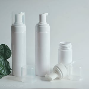 May include: Three white plastic bottles with pump tops. Two bottles are taller and have a clear cap. The third bottle is shorter and has a white cap. The bottles are on a white surface.