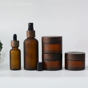 May include: Set of four amber glass bottles with wooden caps. Two bottles have a dropper, one has a spray nozzle, and one is a jar. The bottles are on a white surface.