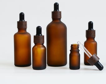 May include: An assortment of amber glass dropper bottles with wooden collars and black droppers. The bottles are of different sizes, with one bottle having a dropper beside it. The text "ONLY4CREATIONS" is visible in the top left corner.
