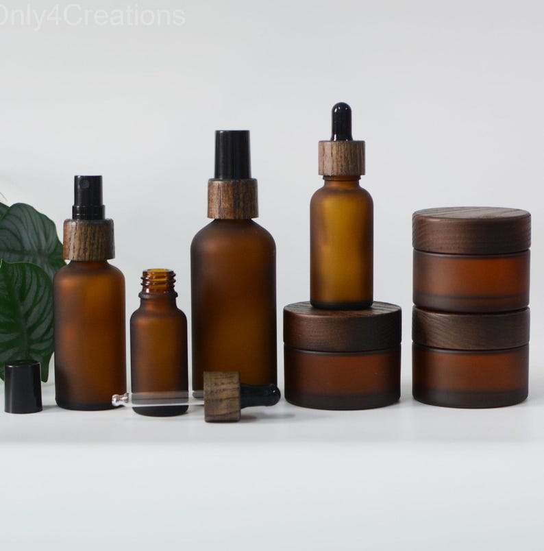 May include: Set of six amber glass bottles with wooden caps and droppers. The bottles are frosted and have a rustic look. The set includes two spray bottles, two dropper bottles, and two jars with wooden lids.