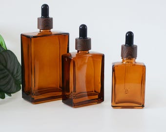 May include: Three amber glass bottles with black dropper tops and wooden caps. The bottles are different sizes and are arranged in a row from largest to smallest.