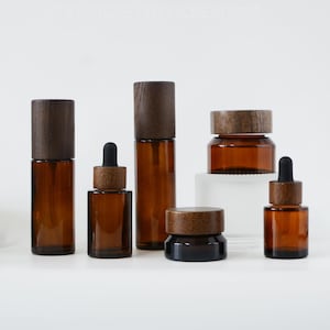 Könnte beinhalten: Satz mit fünf Bernstein-Glasflaschen mit Holzdeckeln. Die Flaschen sind in verschiedenen Größen und Formen, darunter ein Glas, eine Tropfflasche und eine Sprühflasche. Die Flaschen sind alle leer und bereit, mit Ihren Lieblingsprodukten gefüllt zu werden.