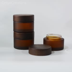May include: Four amber glass jars with wooden lids. The jars are stacked on top of each other. The jars are frosted and have a natural, rustic look.