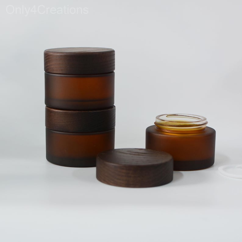 May include: Four amber glass jars with wooden lids. The jars are stacked on top of each other. The jars are frosted and have a natural, rustic look.