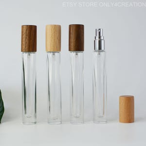 Op de afbeelding: Vijf glazen flessen met houten doppen en een zilveren sproeikop. De flessen zijn helder en hebben een rechthoekige vorm. De houten doppen zijn ofwel lichtbruin of donkerbruin.