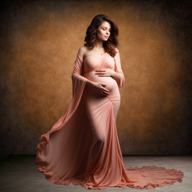 May include: A pregnant woman in a peach-colored, flowing gown with a one-shoulder design. She is standing in front of a brown background and holding her belly.