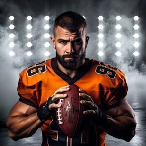 May include: A football player in an orange jersey with the number 66 on it, holding a brown football. He is standing in front of a wall of white lights.