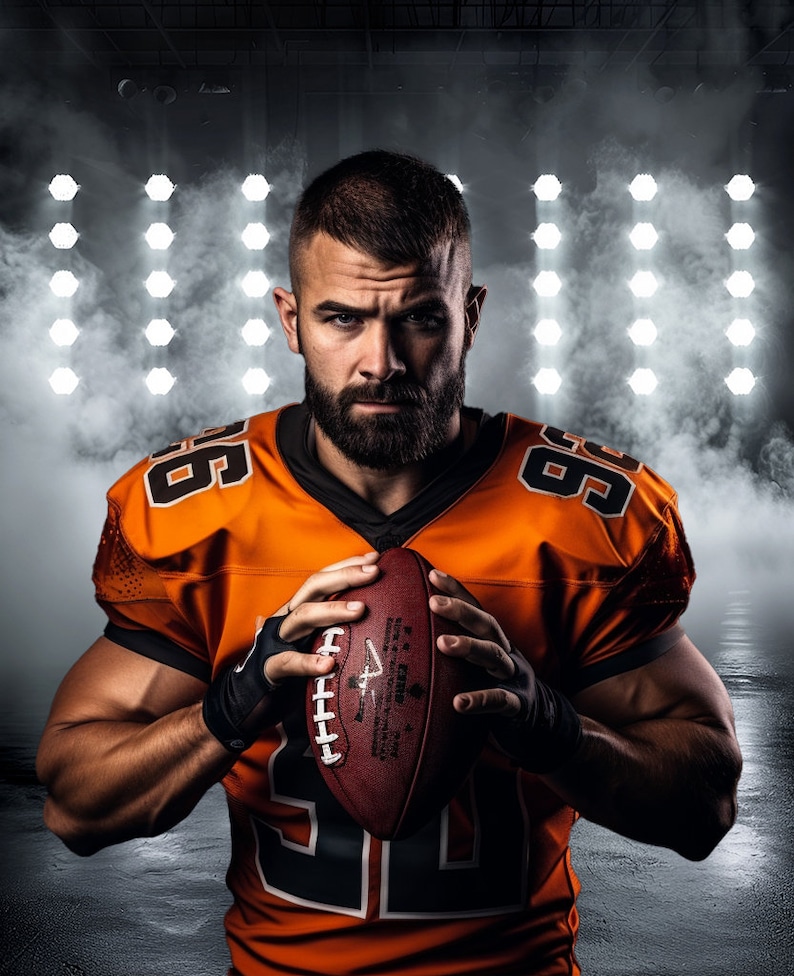 May include: A football player in an orange jersey with the number 66 on it, holding a brown football. He is standing in front of a wall of white lights.