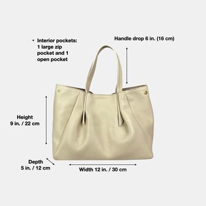 May include: Cream-colored leather tote bag with a handle drop of 6 inches (16 cm). The bag is 9 inches (22 cm) high, 5 inches (12 cm) deep, and 12 inches (30 cm) wide. It has interior pockets, including a large zip pocket and an open pocket.