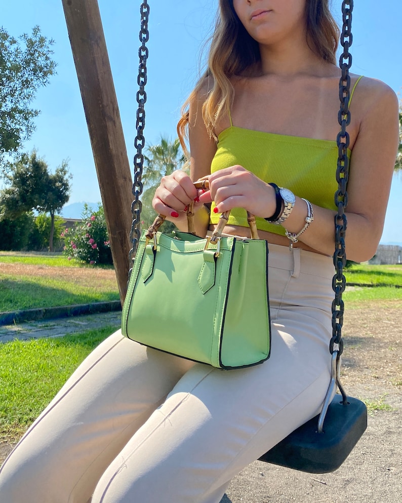 May include: A light green handbag with bamboo handles and a black trim. The bag is small and has a top flap closure.