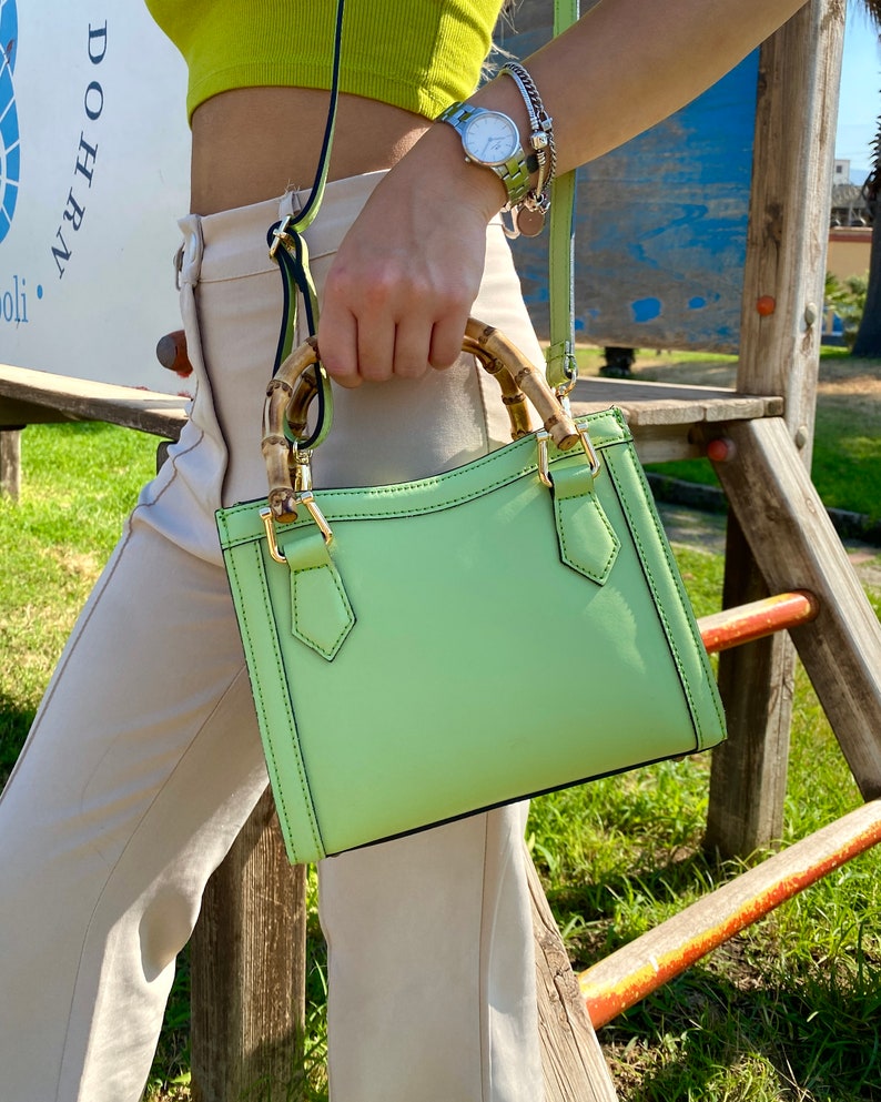 May include: A light green leather handbag with a bamboo handle. The bag has a top flap with a gold buckle closure.