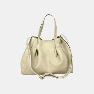 May include: A light beige leather handbag with a textured finish. The bag has two short handles and a long, adjustable shoulder strap. The bag's design features a gathered top and a subtle gold-colored buckle.