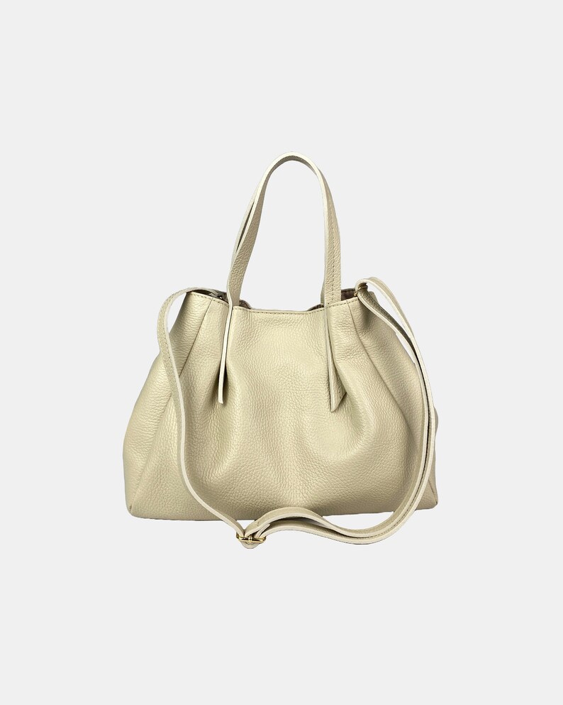 May include: A light beige leather handbag with a textured finish. The bag has two short handles and a long, adjustable shoulder strap. The bag's design features a gathered top and a subtle gold-colored buckle.