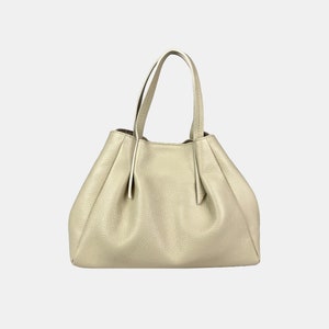 May include: A light beige leather handbag with two handles. The bag has a gathered design and a structured shape. The leather has a textured appearance. The handles are thin and attached to the top of the bag.