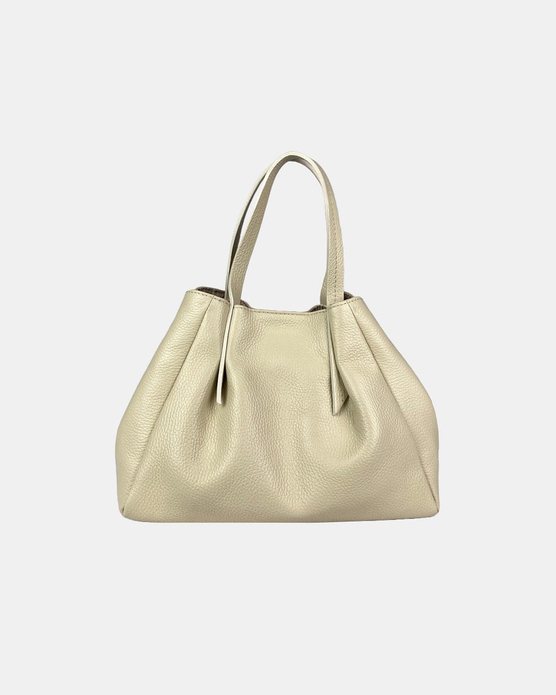 May include: A light beige leather handbag with two handles. The bag has a gathered design and a structured shape. The leather has a textured appearance. The handles are thin and attached to the top of the bag.