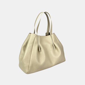 May include: A gold-colored handbag with a textured surface. The bag has a rounded shape with a gathered design and two handles with white accents. The bag is made of a soft material.