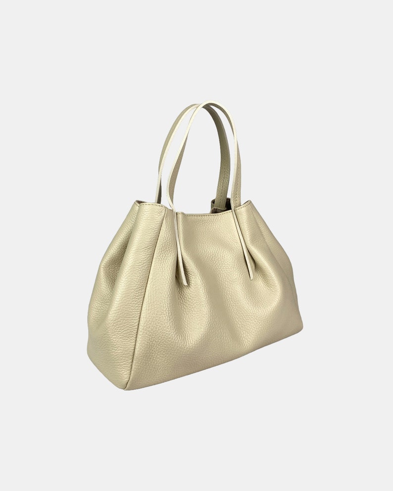 May include: A gold-colored handbag with a textured surface. The bag has a rounded shape with a gathered design and two handles with white accents. The bag is made of a soft material.