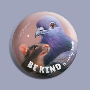 Könnte beinhalten: Ein runder Knopf mit einem Gemälde eines Taubens und einer Ratte. Die Taube ist lila und blau und hat ihren Kopf auf dem Kopf der Ratte ruhen. Die Ratte ist braun und grau. Der Text "BE KIND to every kind" ist in Weiß auf dem Knopf geschrieben.