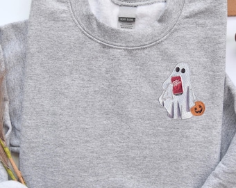 May include: A heather gray sweatshirt featuring a ghost design holding a Dr. Pepper can and a small orange pumpkin. The ghost design is embroidered on the front of the sweatshirt. The sweatshirt has a crew neck and long sleeves.