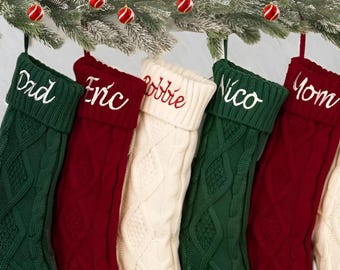 May include: Five personalized Christmas stockings with names embroidered on the cuff. The stockings are made of knitted fabric in green, red, and white.