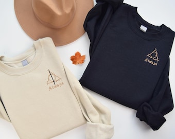 May include: Two long-sleeved sweatshirts with the Deathly Hallows symbol and the word "Always" embroidered on them. One sweatshirt is beige and the other is black.