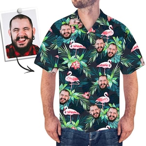 Op de afbeelding: Een kort mouw overhemd met knopen en een tropische print met roze flamingo's, groene bladeren en rode bloemen. Het shirt heeft een herhalend patroon van een menselijk gezicht.