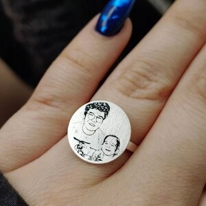 May include: A silver ring featuring a round engraved image of a woman and a child. The image is in black and white.