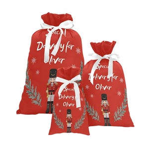 May include: Three red Christmas gift bags with white ribbon and a nutcracker design. The bags are personalized with the text "Special Delivery for Oliver".