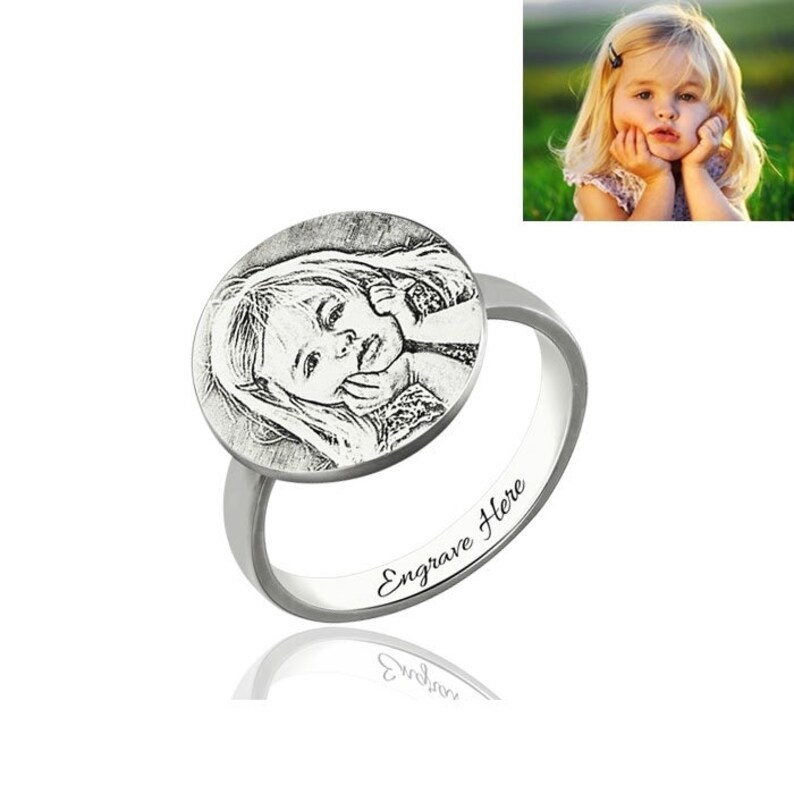 May include: Silver ring featuring a round engraved photo of a young girl. The ring has the words "Engrave Here" inscribed on the band.