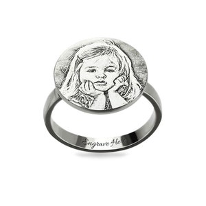 May include: A silver ring featuring a round, engraved photograph of a young girl. The ring has the words "Engrave Here" inscribed on the band.