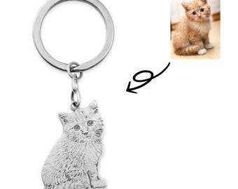 May include: Silver keychain with a photo of a cat engraved on the charm. The keychain has a silver ring and a silver chain.